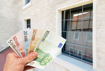 Hand mit Geldscheinen vor Hauswand